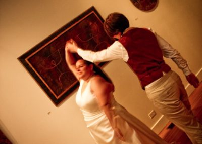 Two women dancing in an art gallery. One wears a white dress; the other wears a suit, minus the jacket.