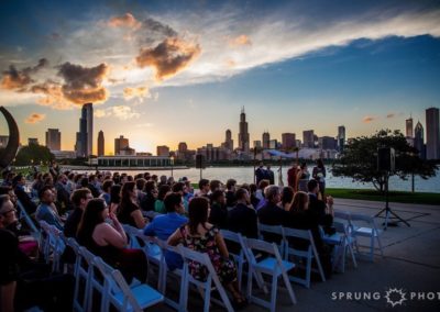 Long view from the side of guests at a wedding. Spectacular view of the Chicago skyline at sunset dominates the photo.