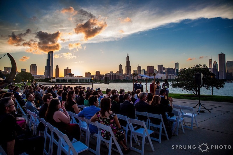 Long view from the side of guests at a wedding. Spectacular view of the Chicago skyline at sunset dominates the photo.