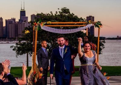 Bride and groom at the head of the recessional, with the chuppah (canopy) behind them. They hold their joined hands high in celebration.