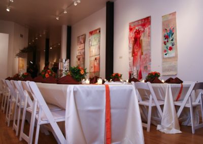 Long banquet tables in an art gallery, decorated in white, orange, and brown.