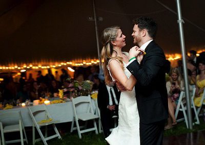 A man in a dark suit and a woman in a white dress dancing on a dance floor in a tent.