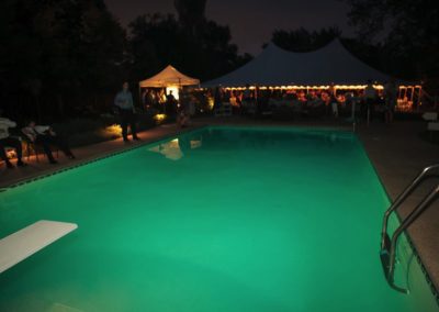 Night shot of a lighted party tent seen over the length of a swimming pool.