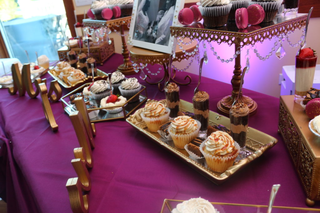 Cupcakes and fancy desserts on gold and mirrored trays on a table with a purple cloth.