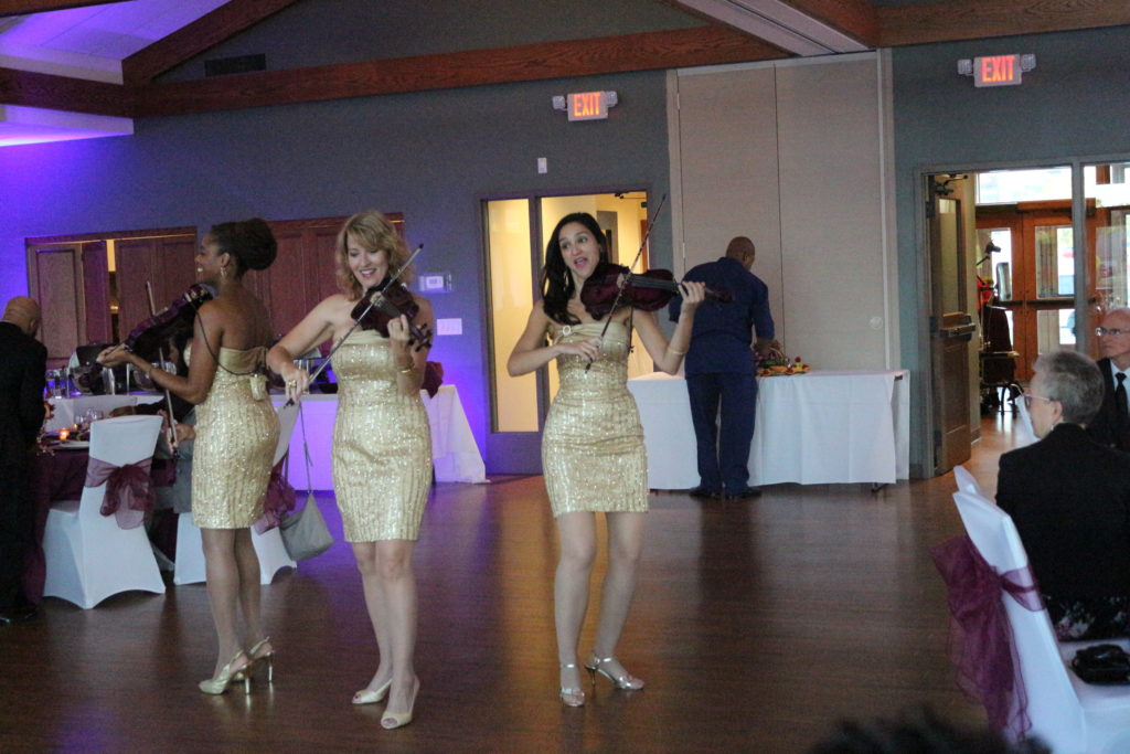 Three women in gold dresses playing violins.