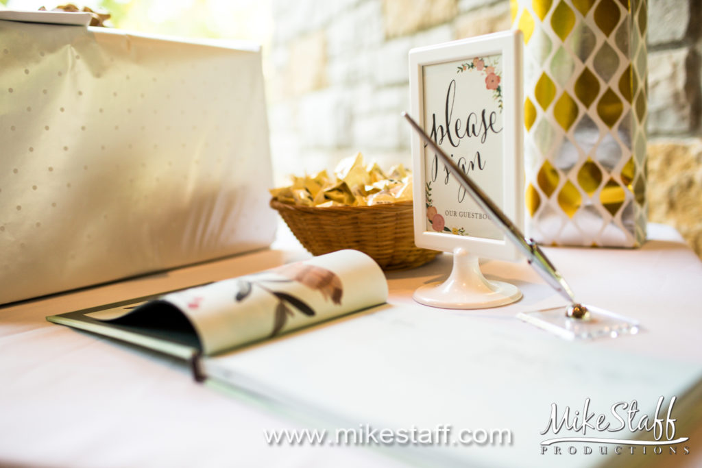 A traditional guest book with pen in holder in front of a sign reading, "Please sign."