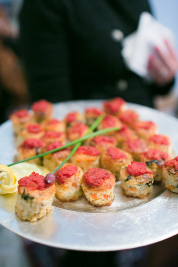 Close-up of a tray of round appetizers, yellowish with a red sauce on top.