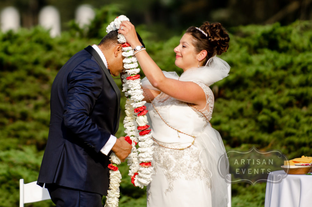 A bride places a flower garland around the neck of her groom.