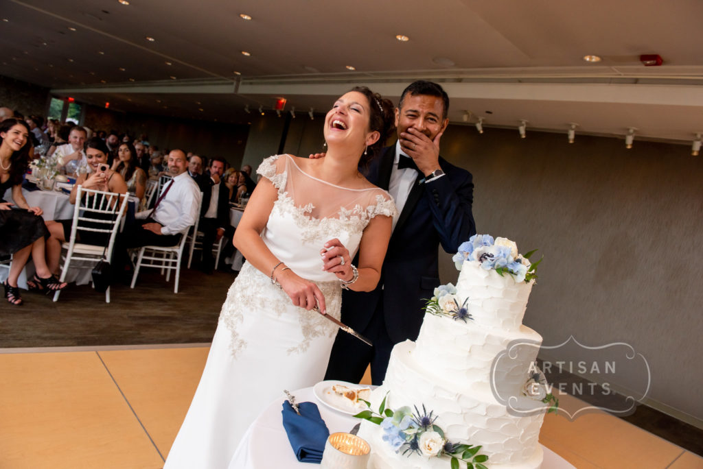 A couple standing near a wedding cake and laughing helplessly.