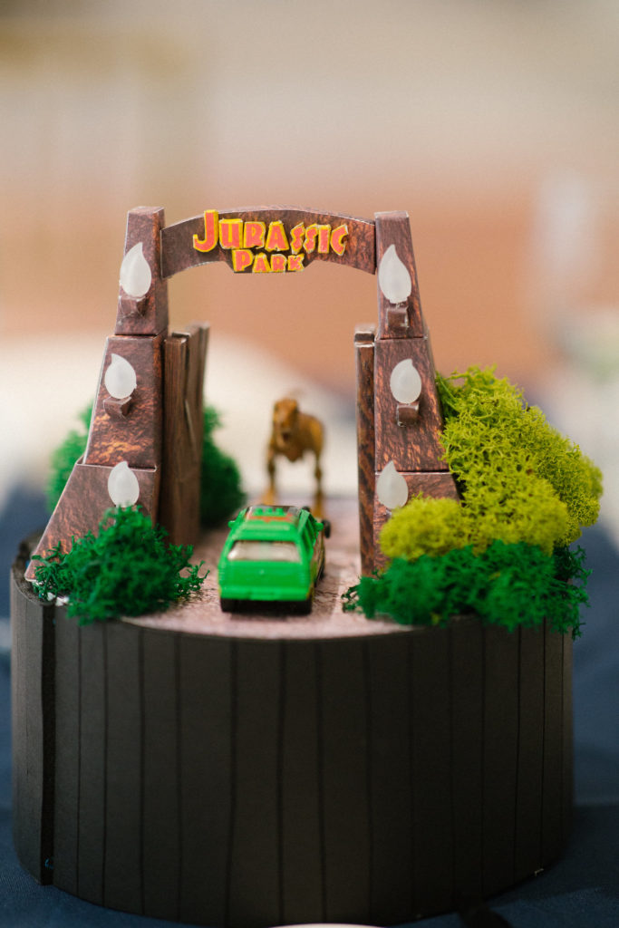 A model of a gateway saying "Jurassic Park," with a green car going in and a dinosaur in the background.