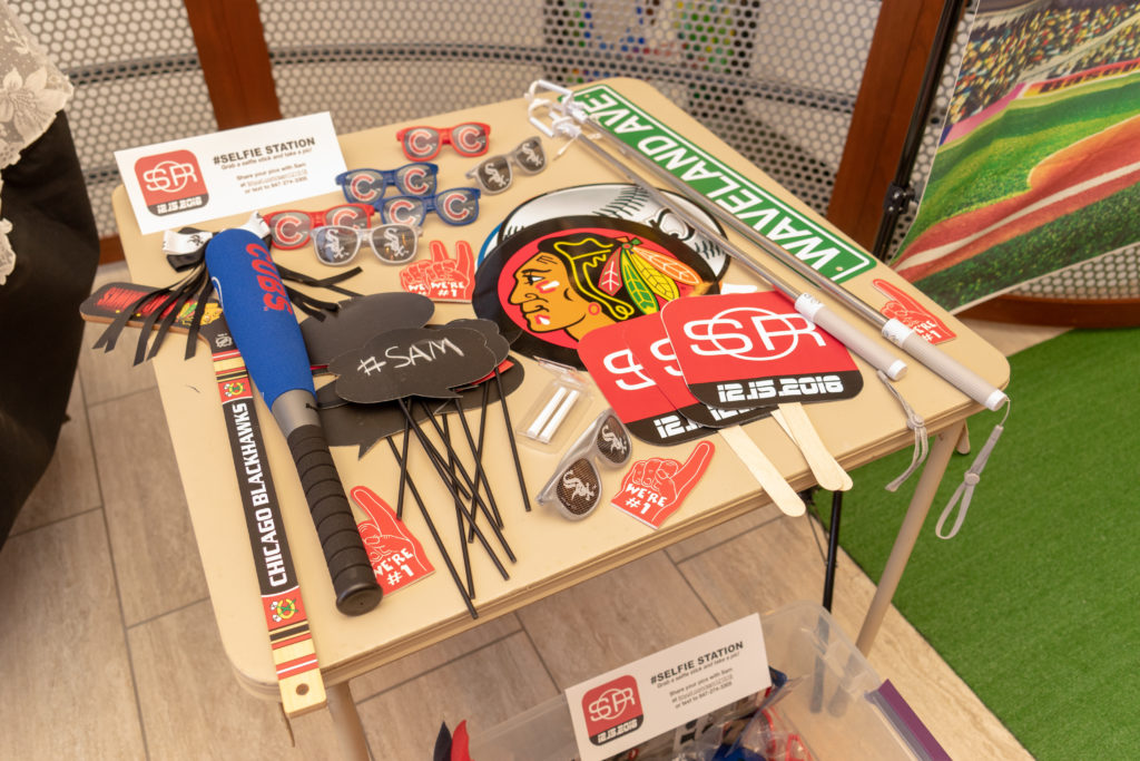 A square table covered in sports-themed selfie photo booth props. Chicago sports teams are featured prominently.