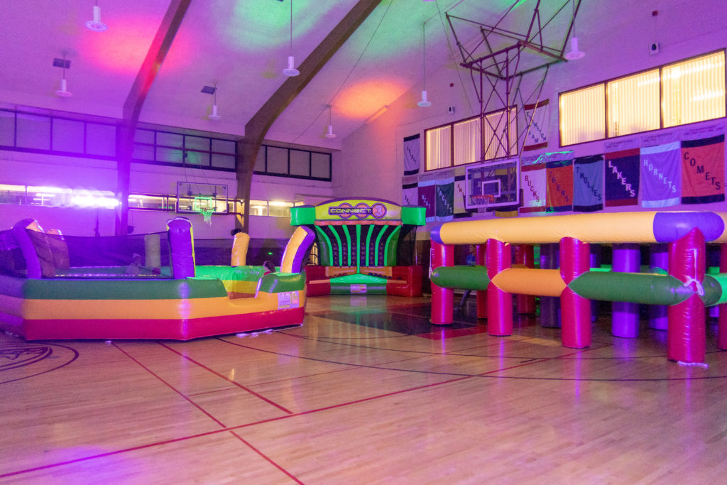 Large, inflatable games in bright colors in a gym, with colored uplighting.