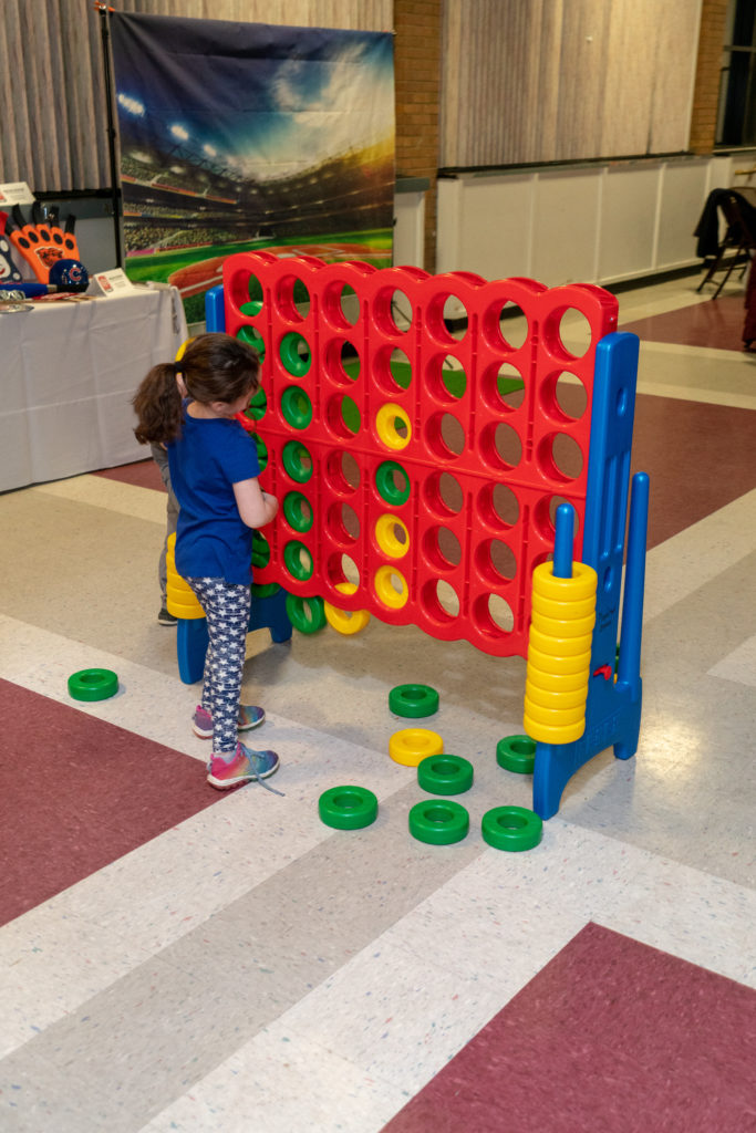 A young person seen from the back playing with a red Connect Four game that is taller than the person.