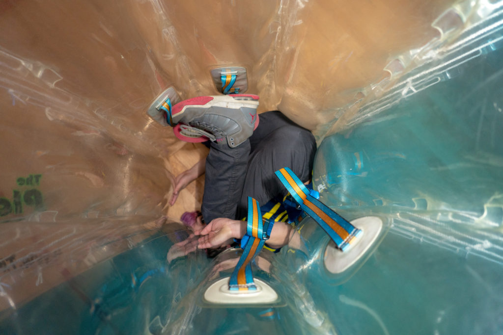 A person curled up inside a large, inflatable ball, with their face invisible.