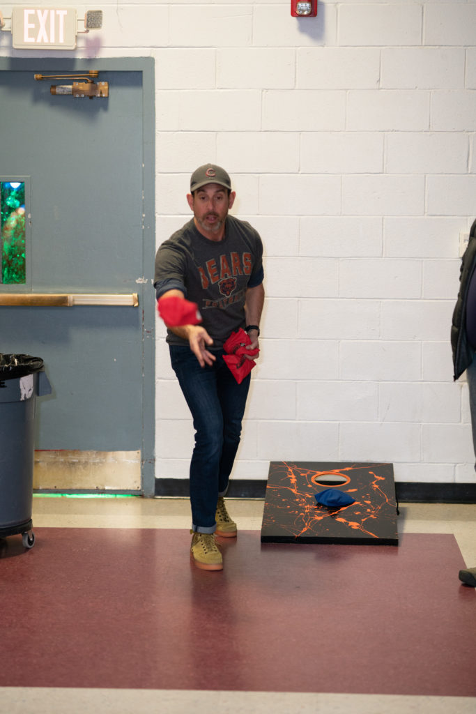 An adult tosses a beanbag in a game of cornhole.
