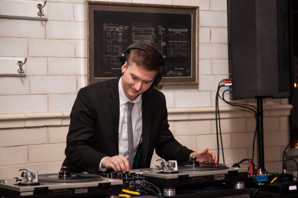 A DJ at work at his turntables, with speakers visible.