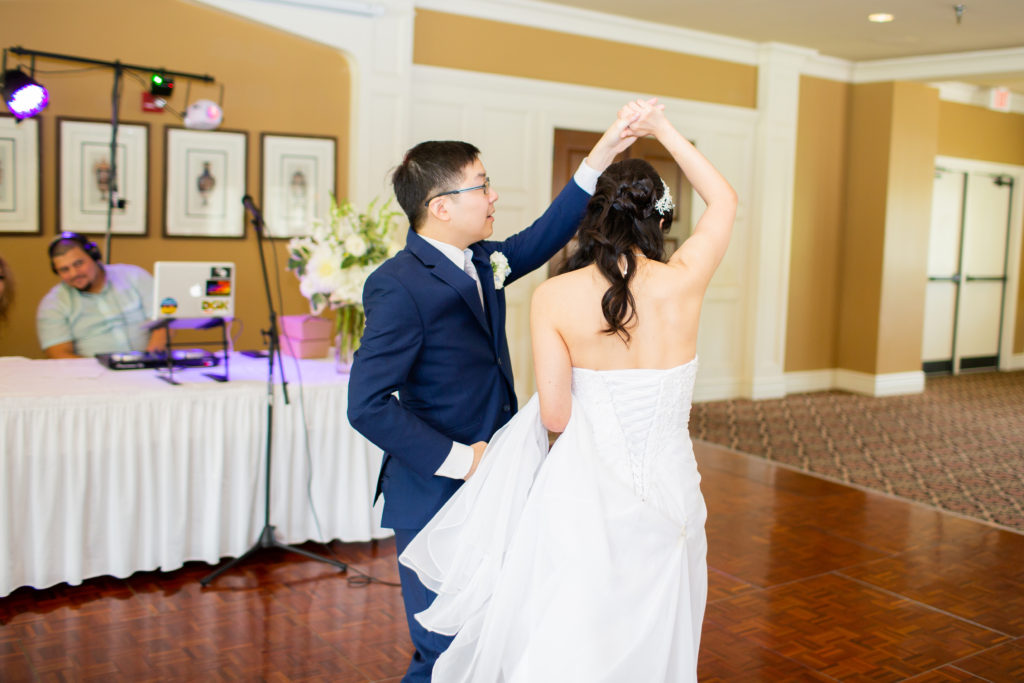 A man in a blue suit and a woman in a white dress dance on a dance floor.