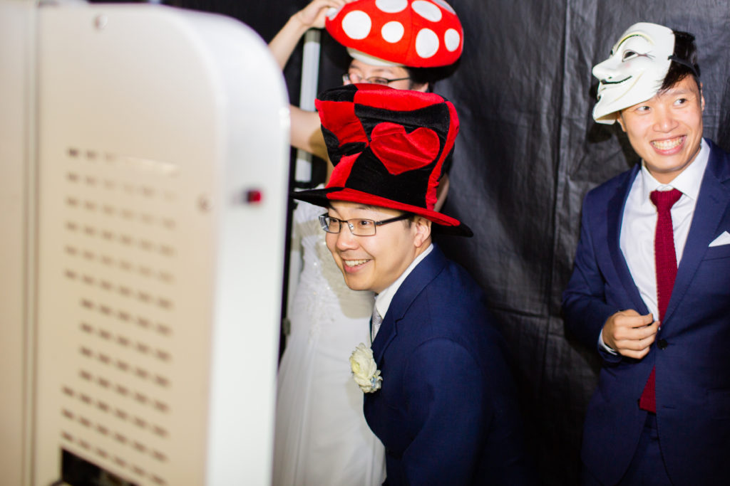 Two men and a woman wearing silly hats and masks in a photo booth.