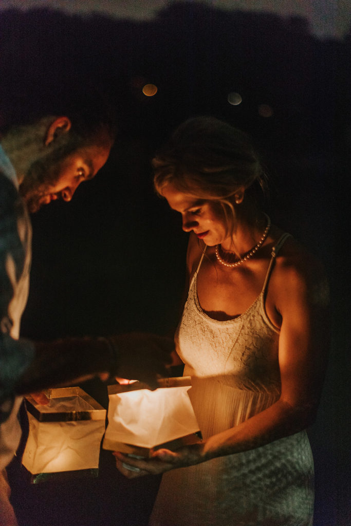 A man and a woman stand face to face in the light of two candle lanterns they are holding between them.