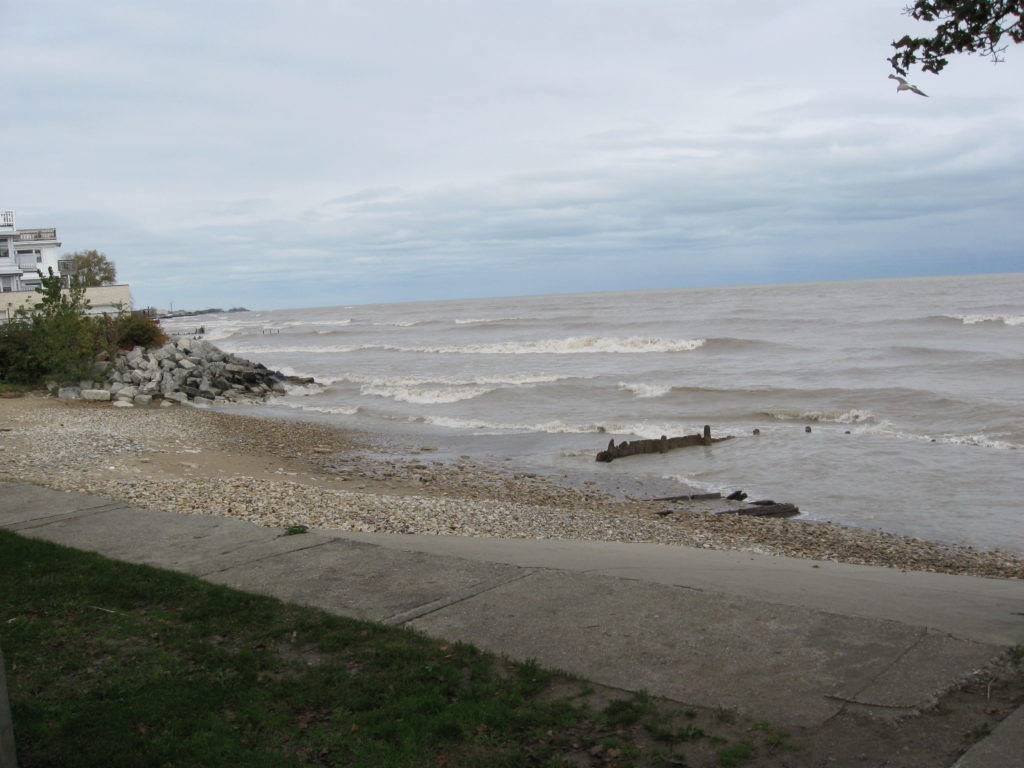 The western shore of Lake Michigan on a gray day. The waves are rather high. There is a building north of the beach in the background.